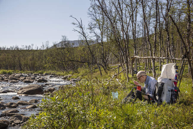 Человек, сидящий у реки во время похода — стоковое фото