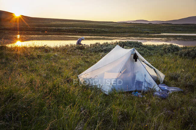 Tenda e uomo campeggio sul fiume durante il tramonto — Foto stock