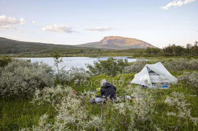 Camping man sitting by river and mountain — Stock Photo