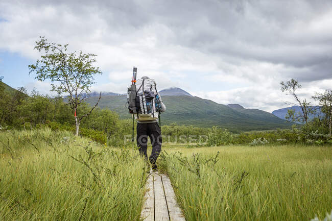 Man hiking on boardwalk to mountains — Stock Photo