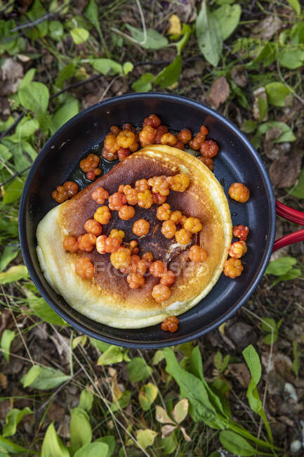 Pancake and cloudberries in frying pan — Stock Photo