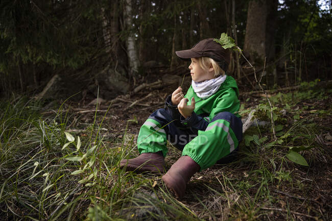 Junge in grüner Jacke sitzt im Wald — Stockfoto