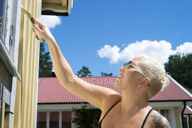Mulher sorridente com óculos de sol pintando casa — Fotografia de Stock