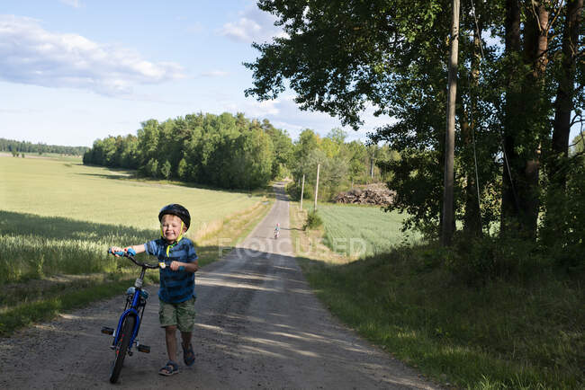 Chico caminando bicicleta en camino rural - foto de stock