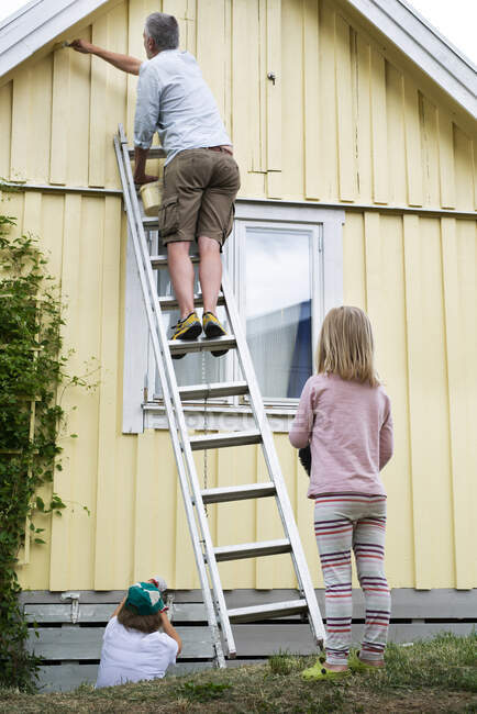 Homme sur échelle peinture maison avec sa famille — Photo de stock