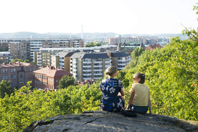 Frau und Teenager sitzen auf einem Felsen über der Stadt — Stockfoto