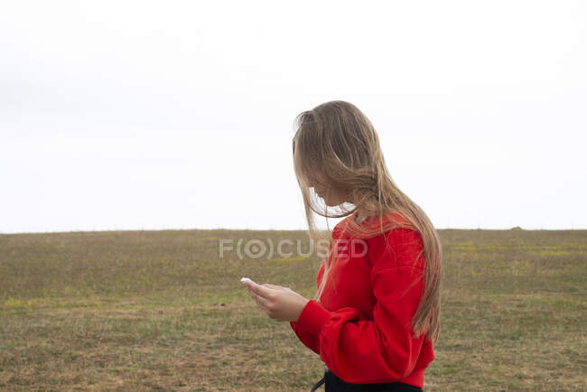 Teenage girl with red sweater text messaging in field — Stock Photo