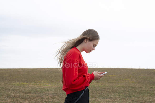 Teenage girl with red sweater text messaging in field — Stock Photo