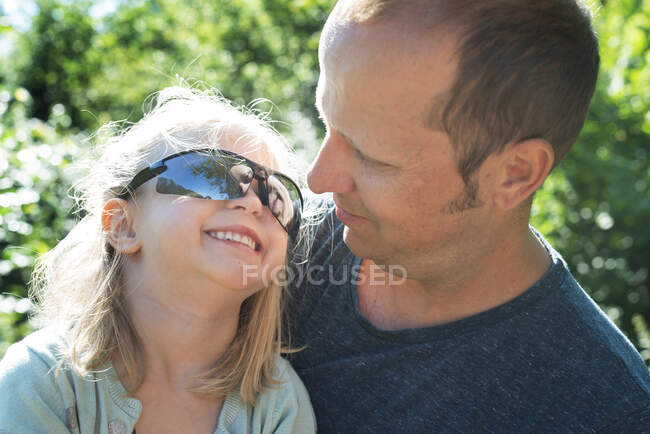Girl with sunglasses sitting with her father — Stock Photo