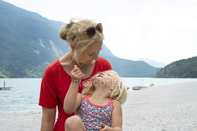 Madre e hija sentadas en la playa - foto de stock