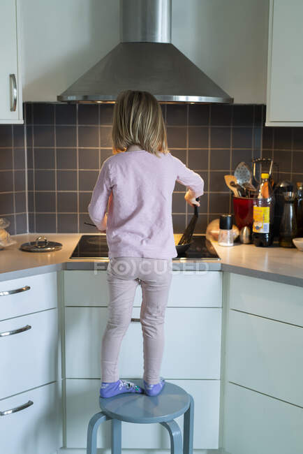 Дівчина стоїть на стільці під час приготування їжі — стокове фото