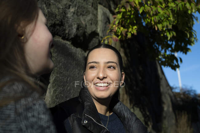 Young woman talking to her friend by stone wall — Stock Photo