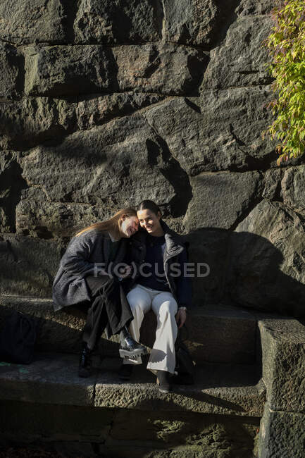 Giovani donne sedute vicino al muro di pietra — Foto stock