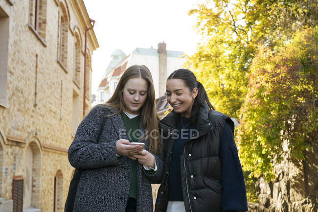 Mujeres jóvenes usando teléfono inteligente en la calle de la ciudad - foto de stock