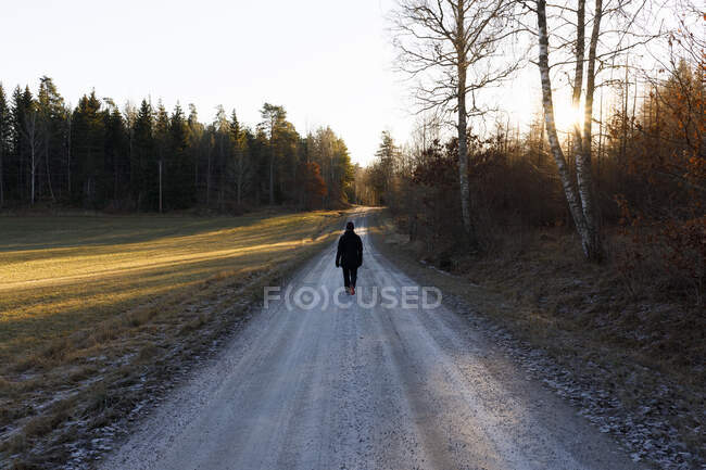 Жінка ходить по сільській дорозі на заході сонця — стокове фото