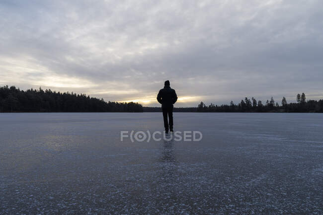 Человек идет по замерзшему озеру на закате — стоковое фото