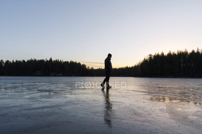 Homem caminhando no lago congelado ao pôr do sol — Fotografia de Stock