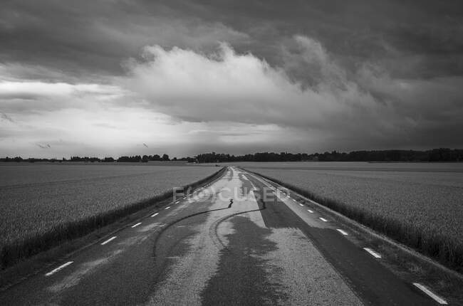 Nuvole su strada rurale e campo — Foto stock