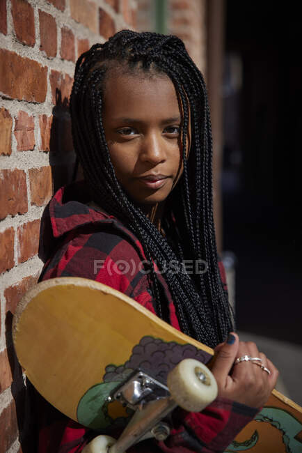 Teenage girl holding skateboard while leaning on brick wall — Stock Photo