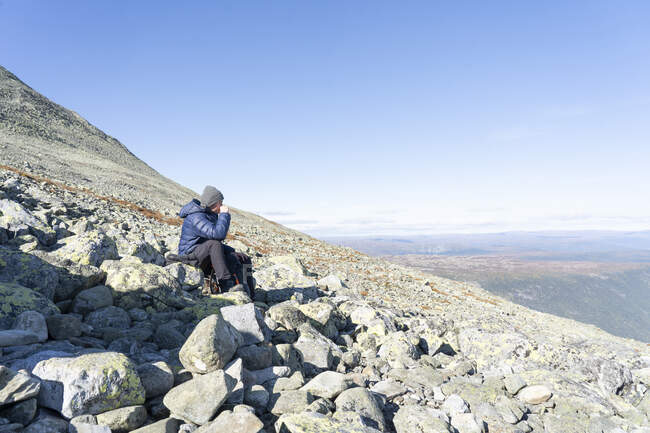 Uomo in giacca blu seduto sulla montagna — Foto stock