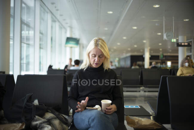 Mulher com xícara de café e smartphone sentado no aeroporto — Fotografia de Stock