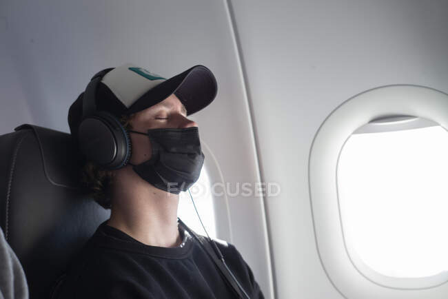 Молодой человек в маске гриппа сидит в самолете — стоковое фото