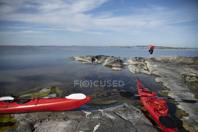 Kayaks rojos y el hombre tomando fotografías en rocas costeras - foto de stock