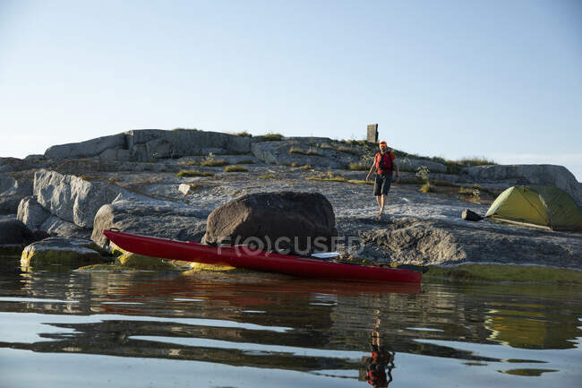Caiaque vermelho e homem acampando em rochas costeiras — Fotografia de Stock