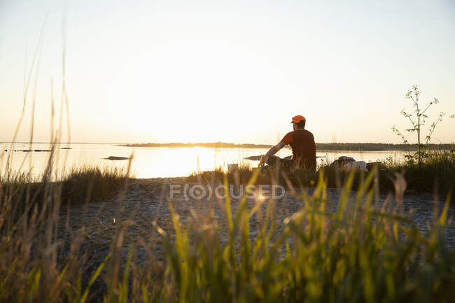Hombre sentado junto al mar al atardecer - foto de stock