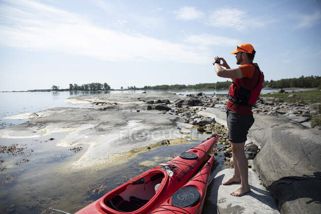 Uomo con kayak rossi sulle rocce costiere — Foto stock