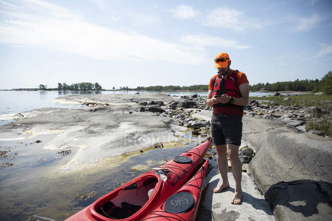 Homme avec des kayaks rouges sur les rochers côtiers — Photo de stock