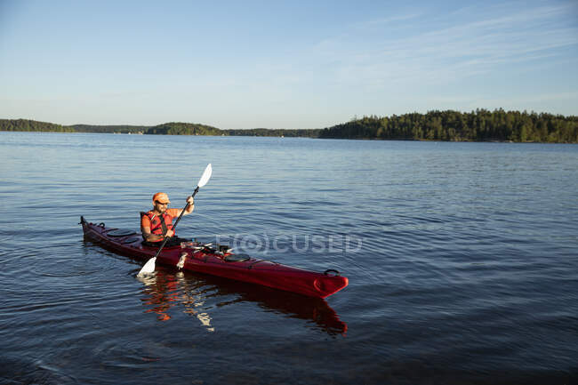 Mann in Schwimmweste paddelt auf See — Stockfoto