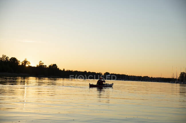 Mann paddelt bei Sonnenuntergang auf See — Stockfoto