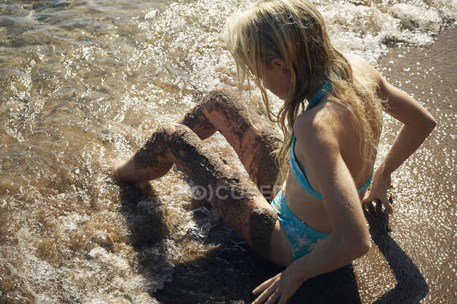 Girl in swimsuit sitting in water at beach — Stock Photo