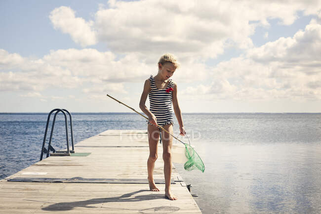 Girl in striped swimsuit with fishing net on jetty — Stock Photo
