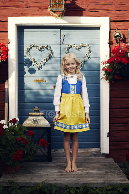 Menina em vestido tradicional de pé na porta para casa — Fotografia de Stock