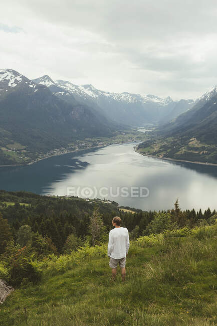 Hombre de pie en la colina por las montañas y el lago - foto de stock