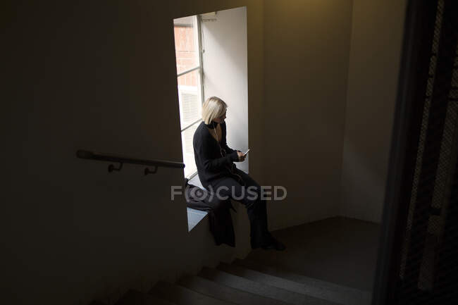 Mujer joven escuchando música en el alféizar de la ventana - foto de stock