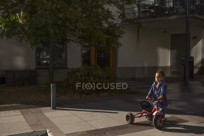 Chica jugando con triciclo por casa - foto de stock
