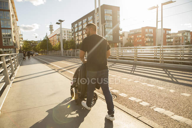Мужчина толкает дочь в коляске на мосту — стоковое фото