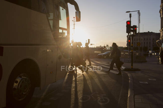 Люди, переходящие дорогу и автобусы на закате — стоковое фото