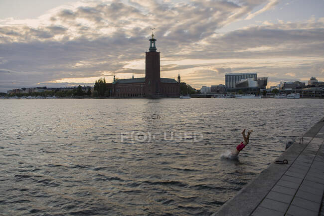Hombre sumergiéndose en el agua por el Ayuntamiento de Estocolmo, Suecia - foto de stock