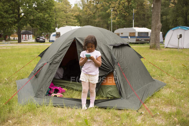 Девушка со смартфоном у палатки во время похода — стоковое фото