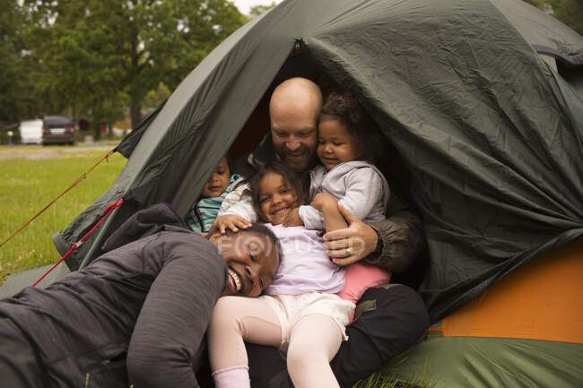 Abrazos familiares en tienda de campaña mientras acampan - foto de stock