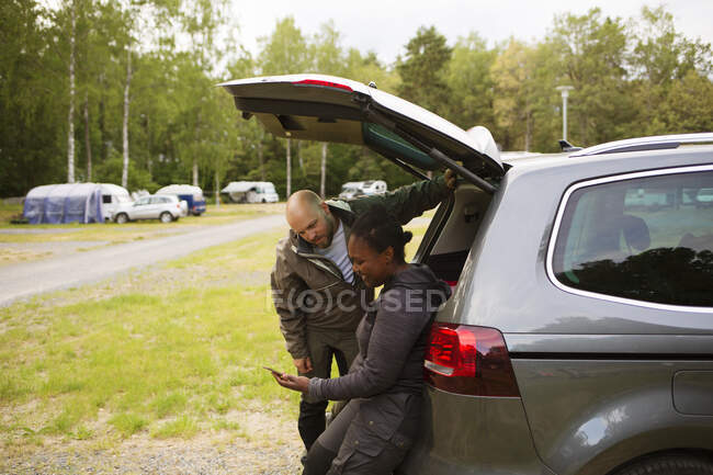 Man and woman looking at smartphone by car — Stock Photo