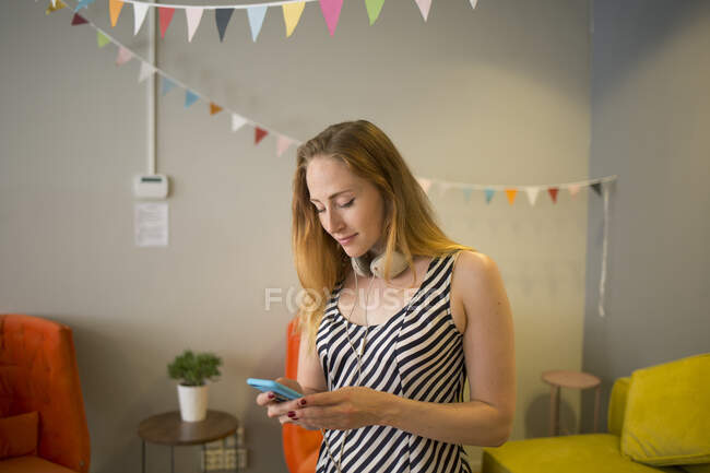 Молода жінка з навушниками тримає смартфон — стокове фото