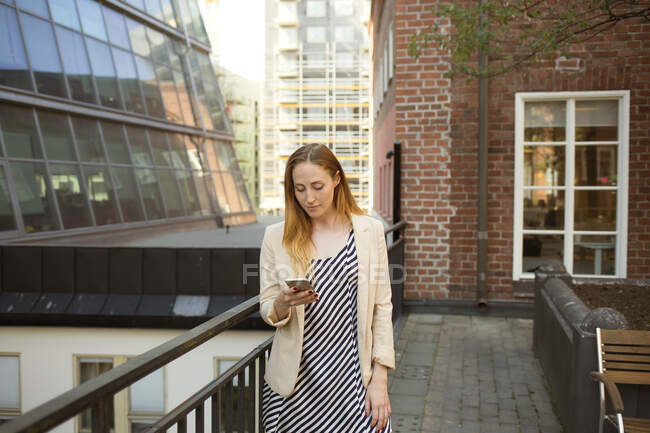 Молодая женщина со смартфоном на балконе — стоковое фото
