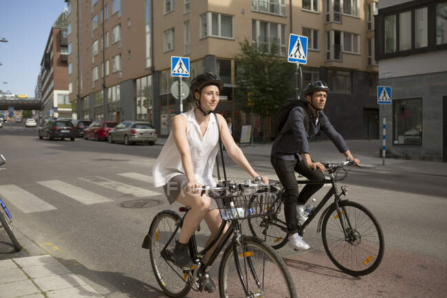 Joven hombre y mujer montando bicicletas en la calle de la ciudad - foto de stock