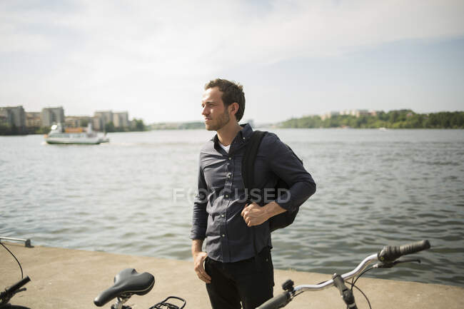 Jeune homme debout au bord de l'eau avec vélo — Photo de stock