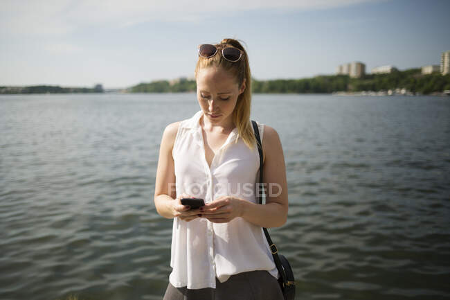 Jeune femme utilisant smartphone par front de mer — Photo de stock